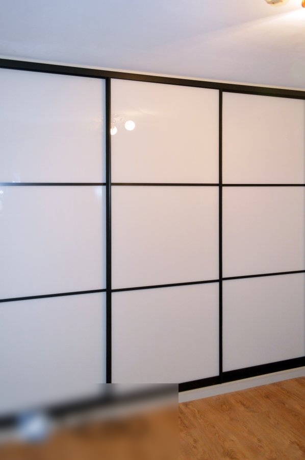 Трехдверный встроенный шкаф-купе в черном профиле с заполнением дверей из белого лакобеля и черными горизонтальными разделениями