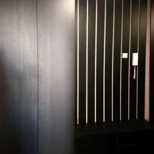 Мебель в прихожую в темных тонах со шкафом для одежды, открытой тумбой-обувницей для сиденья и вешалкой из реек с вырезами под домофон и выключатель