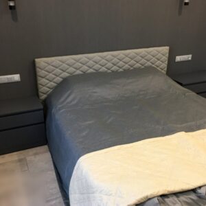 Двуспальная кровать с мягкой спинкой и двумя прикроватными тумбочками с выдвижными полками