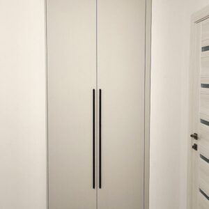 Встроенный в нишу шкаф до потолка с черными длинными ручками в спальне